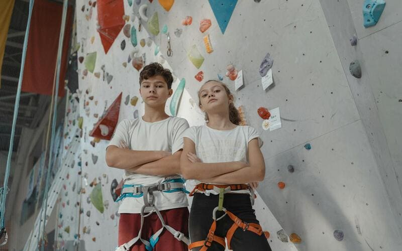 Two kids standing next to rock climbing wall